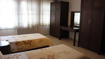 A hotel room with two beds, a desk, a wardrobe, and a mirror.