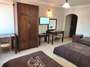 Quarto de hotel com duas camas, uma escrivaninha, uma cadeira, um guarda-roupa e uma televisão mostrando a mensagem "WELCOME".