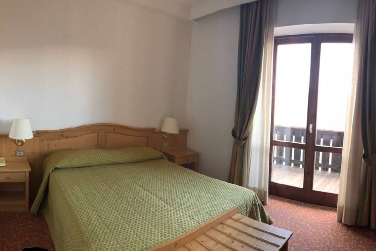 A hotel room with a bed, bedside tables, a television, and a balcony with curtains.