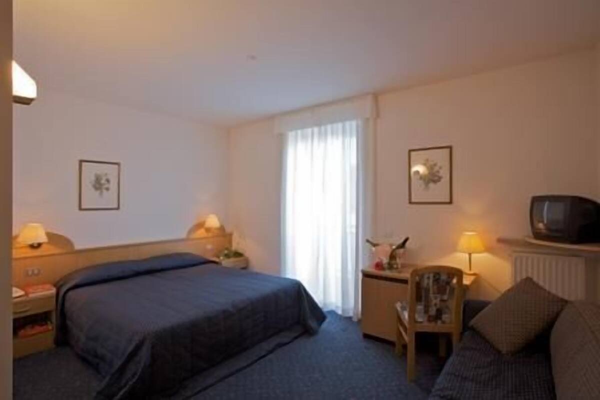 A hotel room with a bed, a chair, a table, a TV, and two lamps.