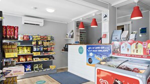 L'intérieur d'une épicerie, avec des étagères remplies de divers produits alimentaires, un rayon de produits surgelés et des affiches promotionnelles.