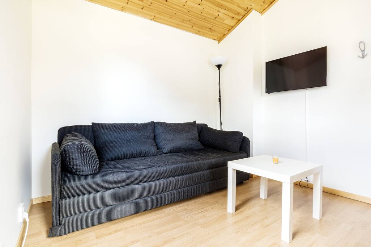 A modern living room with a grey sofa, a white coffee table, and a flat-screen TV mounted on the wall.