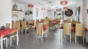 L’intérieur d’un restaurant, avec des chaises et des tables en bois, des nappes rouges et une statue de Bouddha accrochée au mur.