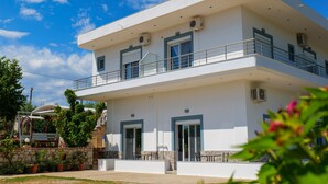 Un edificio moderno de dos pisos con balcón, ventanas grandes y mobiliario exterior.