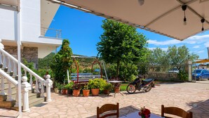 Un patio con mesa, sillas, plantas en macetas, un banco y una escalera que sube a un nivel superior.