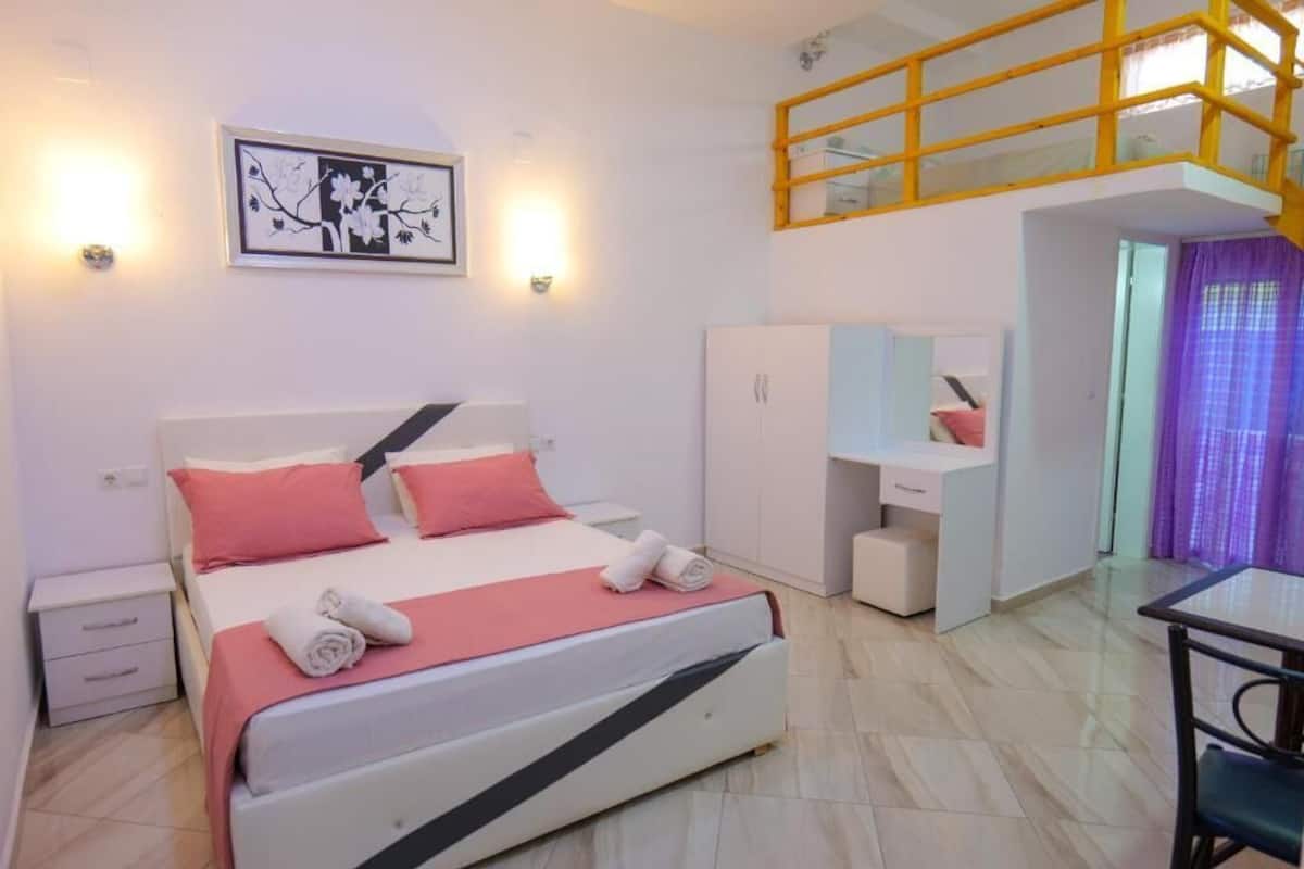 A bedroom with a bed, a nightstand, a desk, a wardrobe, and a staircase.