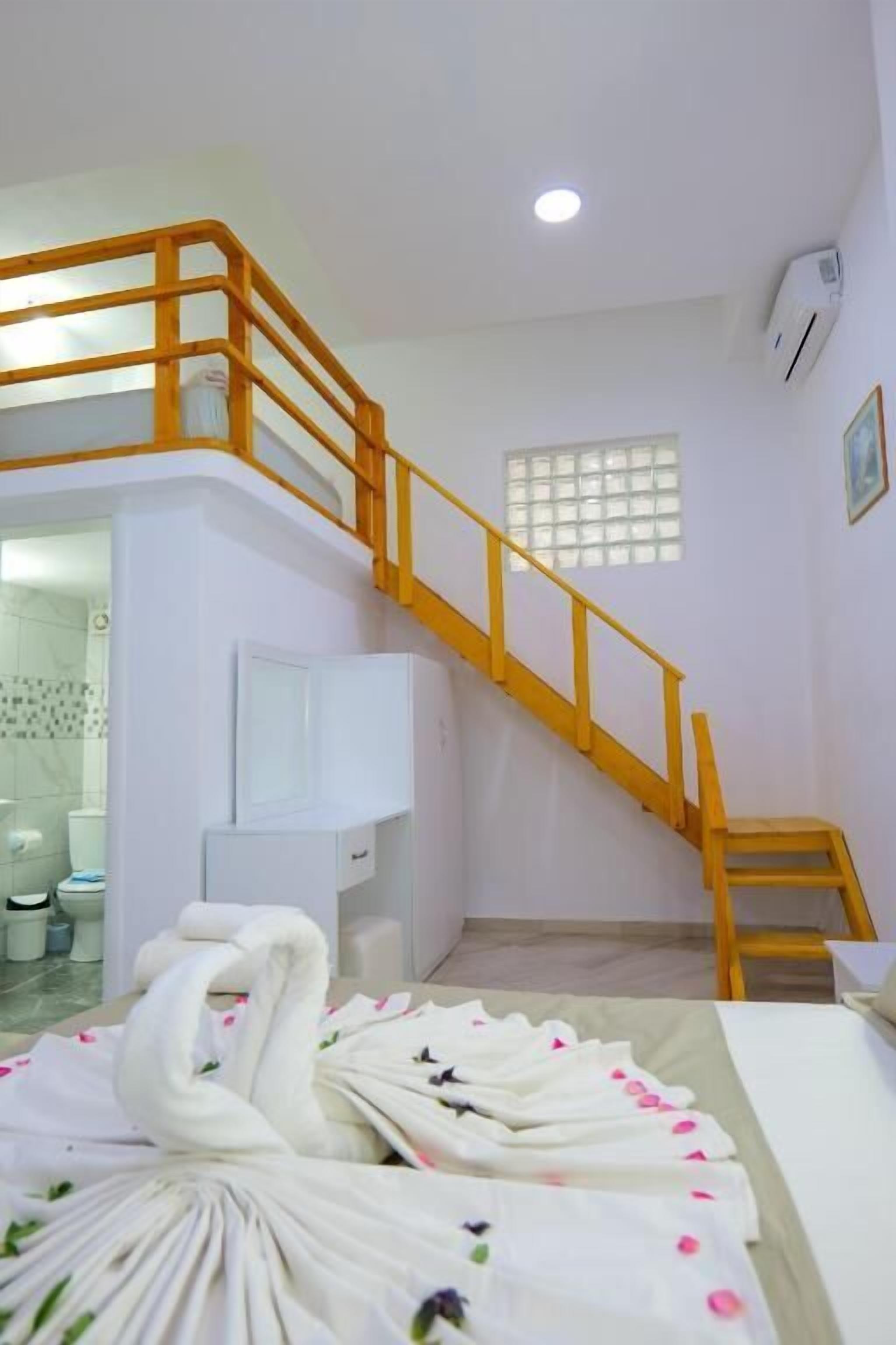 A hotel room with a wooden staircase, a bed with white linens and floral patterns, a white cabinet, and a window with a grid pattern.