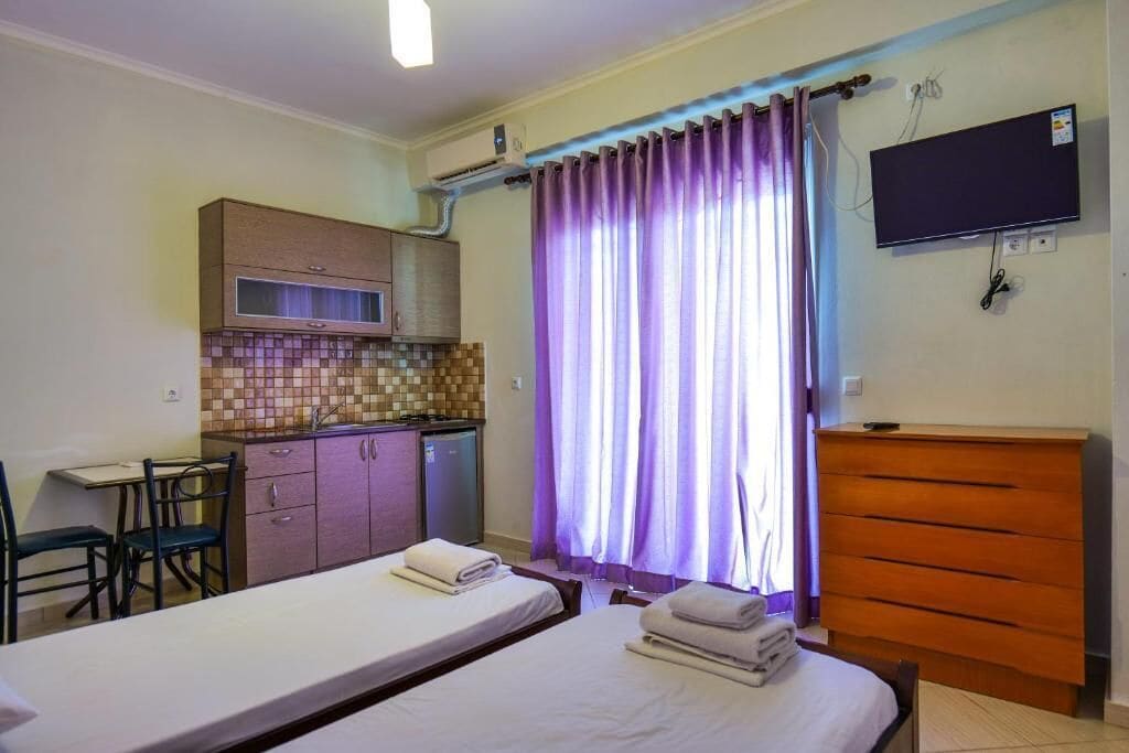 A hotel room with a bed, a desk, a small kitchenette, and a TV.