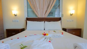 Una cama bien hecha con un arreglo floral y toallas, un cabecero de madera, lámparas de noche y una ventana con cortinas.