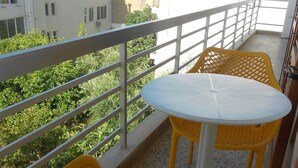 A balcony with yellow wicker chairs and a white table, overlooking a building and greenery. - Paradise City (Rethymno)