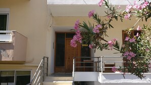 A building with a staircase leading to a door, a balcony with a railing, and pink flowers in the foreground. - Paradise City (Rethymno)