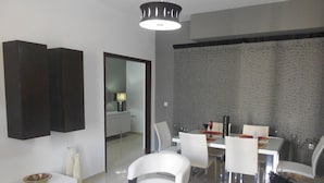 A modern living room with a dining area, featuring a glass table, white chairs, and a dark-toned sofa. - Paradise City (Rethymno)
