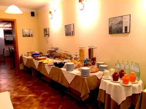 Montaje de bufé con distintos alimentos y bebidas, suelo de baldosas y una pared decorada con cuadros.