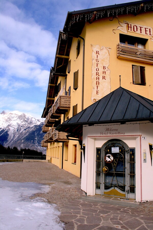 Un hotel con montañas al fondo, un letrero que dice "Hotel Santellina" y un letrero que indica "Ristorante Bar Ristorante".