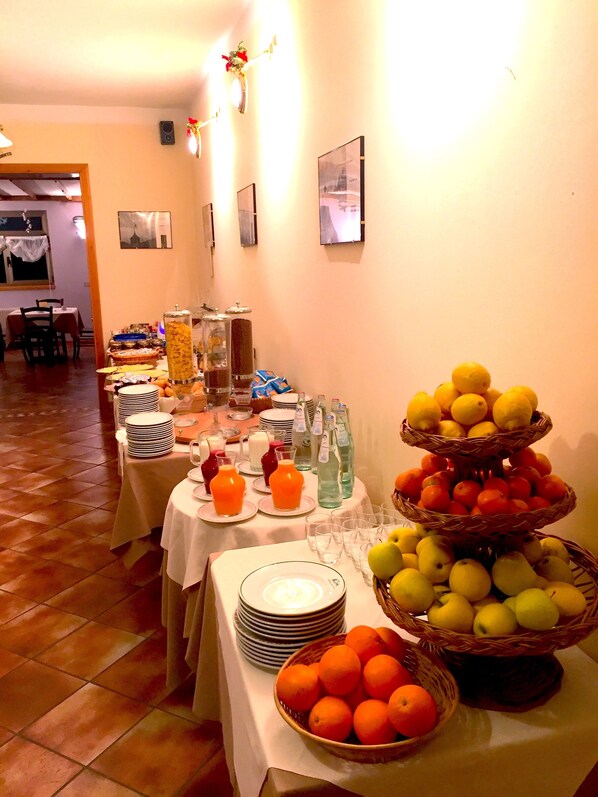Montaje de bufé con diversos alimentos y bebidas, incluyendo frutas y jugos, dispuesto en mesas.