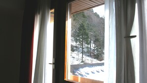 Ein Fenster mit Vorhängen, Blick auf eine verschneite Landschaft mit Bäumen und ein Holzgebilde im Freien.