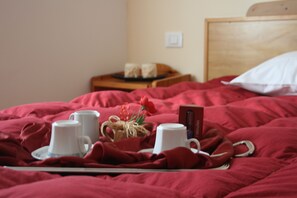 Una cama bien tendida con una bandeja de tazas blancas y un pequeño objeto decorativo sobre un edredón rojo.