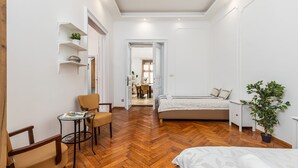 Un dormitorio con piso de madera en patrón de espiga, una cama, una mesita de noche, una silla, una pequeña mesa con un libro y una planta en maceta.