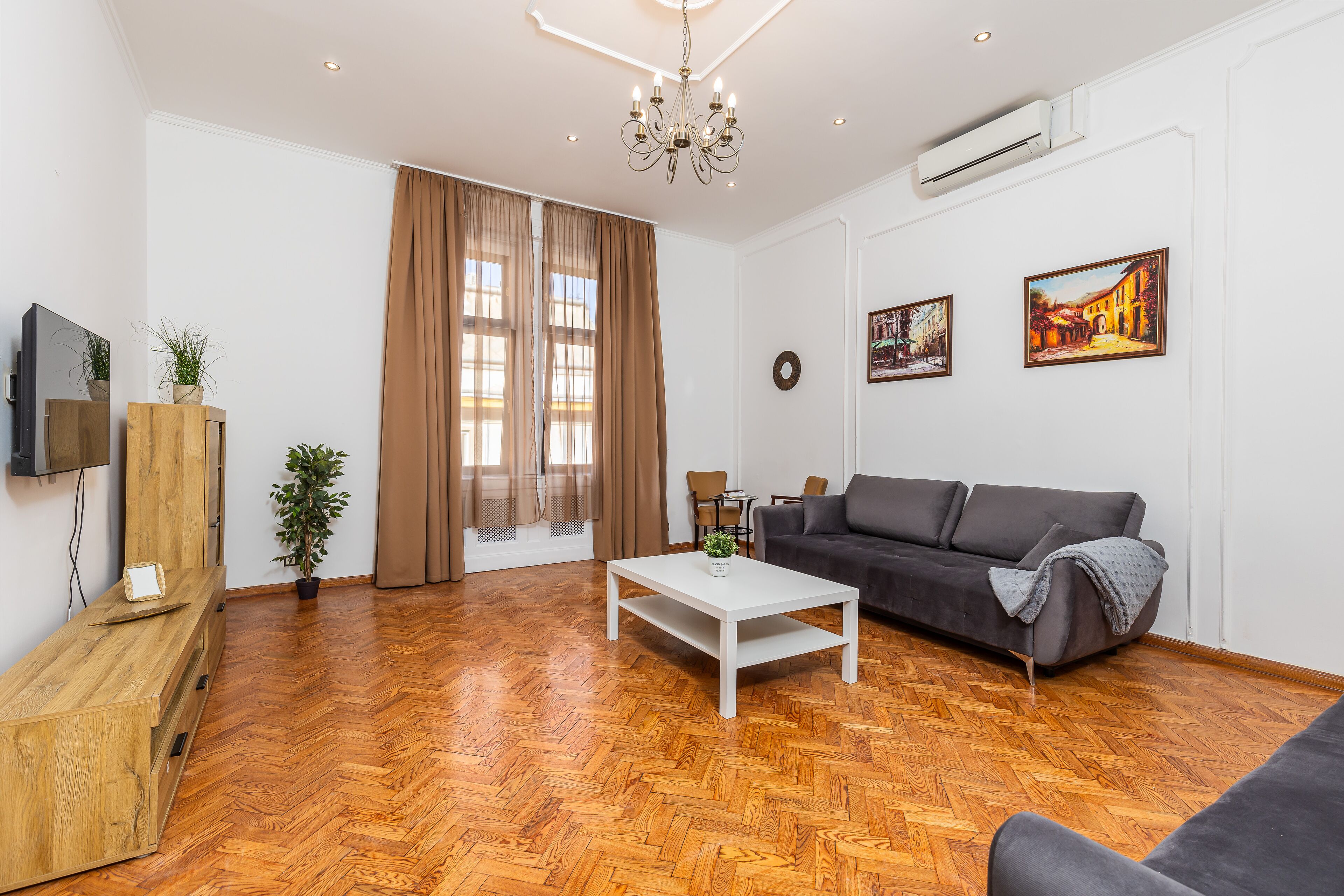 Una sala de estar moderna con suelo de parqué labrado, un sofá gris, una mesa de centro blanca y una araña.
