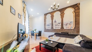 A modern living room with a large window, a flat-screen TV, a sofa, a coffee table, and a red rug. - Real Apartments Anker koz (Budapest)