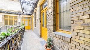 A corridor with yellow doors and windows, brick walls, and a metal railing with potted plants. - Real Apartments Anker koz (Budapest)