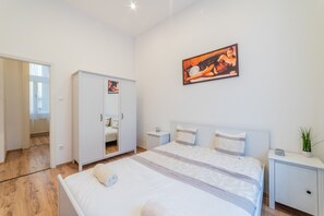 A modern bedroom with a large bed, a wardrobe, a bedside table, and a wall-mounted artwork. - Real Apartments Anker koz (Budapest)