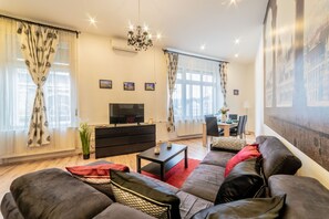 A modern living room with a sofa set, a TV, a dining area, and a chandelier. - Real Apartments Anker koz (Budapest)