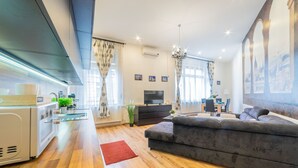 A modern living room with a sofa, TV, and kitchen area with a microwave. - Real Apartments Anker koz (Budapest)