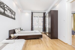 Un dormitorio moderno con dos camas, un ventanal grande y un armario oscuro.