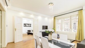 Un área de comedor con una mesa, sillas, un jarrón con flores y un televisor al fondo.