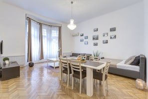 A modern living room with a dining table, chairs, a sofa, and a chandelier. - Real Apartments Lovag (Budapest)