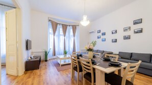 A modern living room with a dining area, wooden flooring, a grey sofa, and a chandelier. - Real Apartments Lovag (Budapest)