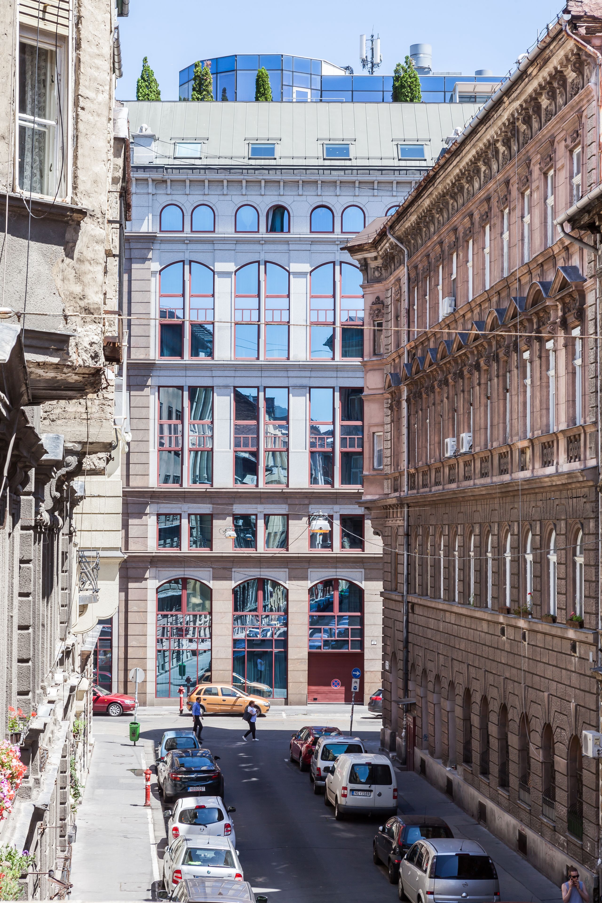A street view with parked cars, a building with large windows, and a modern structure above.