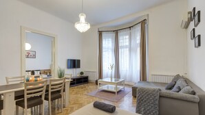 A well-lit room with a dining table, chairs, a sofa, and a TV. - Real Apartments Lovag (Budapest)
