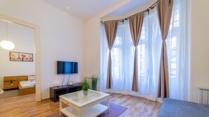 A modern living room with a glass coffee table, a sofa, a TV, and a bed with a wooden headboard. - Real Apartments Lovag (Budapest)