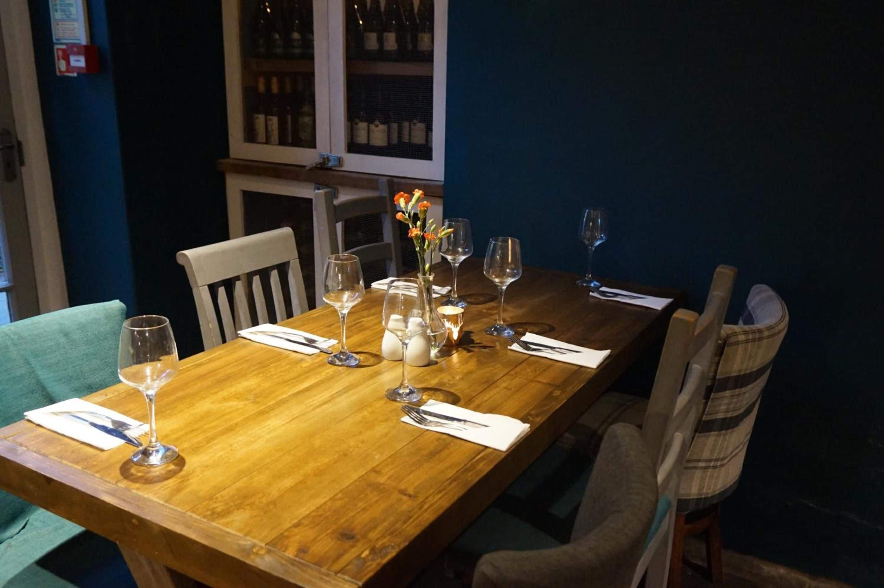 A wooden dining table set with wine glasses, a vase with flowers, and a candle.