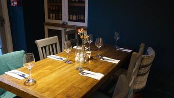 A wooden dining table set with wine glasses, a vase with flowers, and a candle.