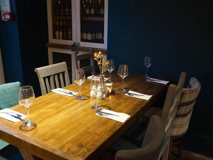 A wooden dining table set with wine glasses, a vase with flowers, and a candle.