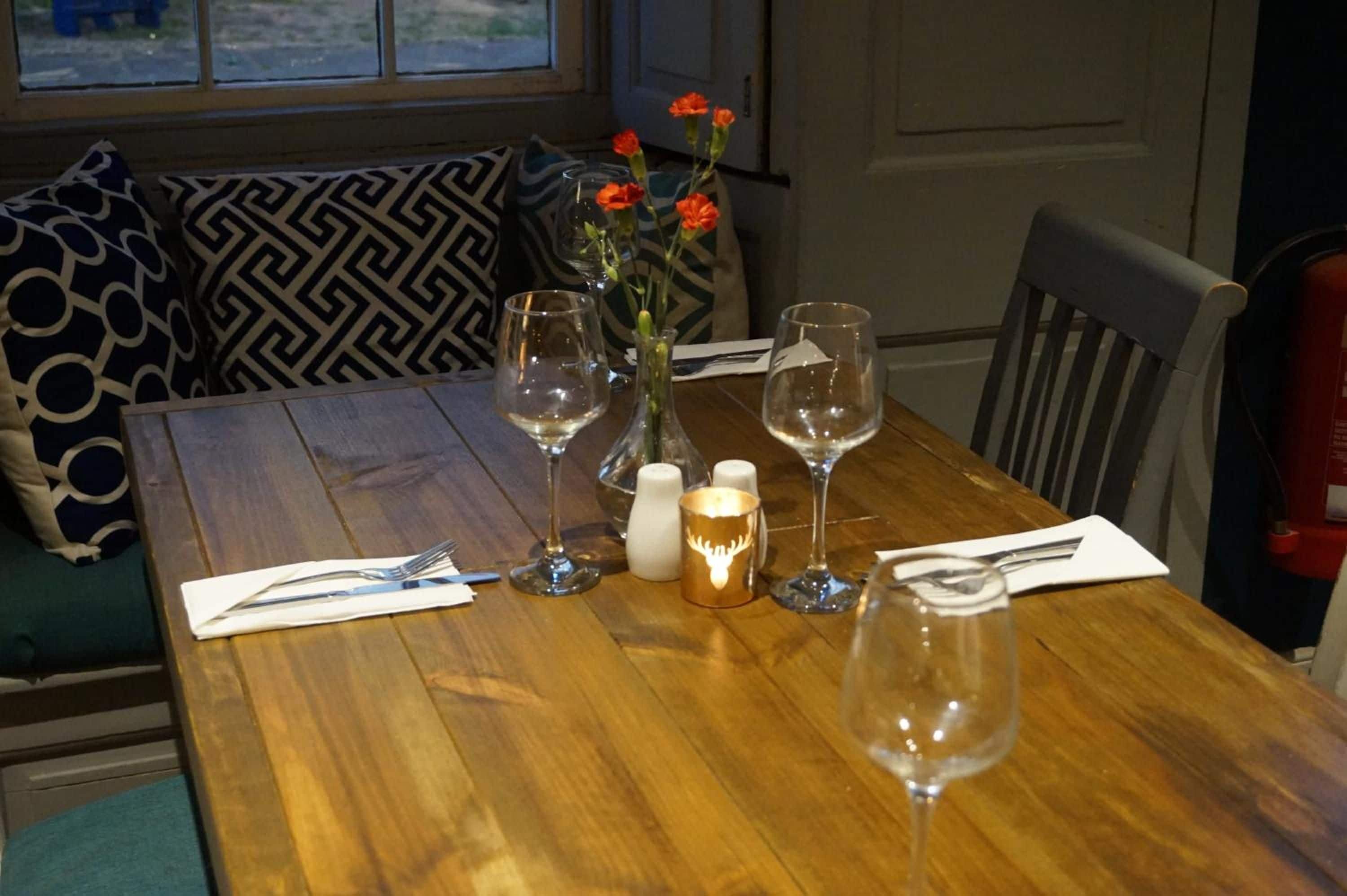 Mesa de comedor dispuesta con copas de vino, un florero con flores, saleros y pimenteros, y una vela.