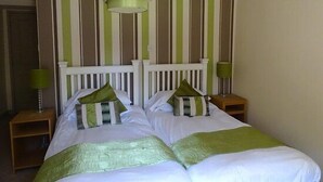 Una cama bien hecha con ropa de cama verde y blanca, un cabecero blanco y una lámpara colgante verde.