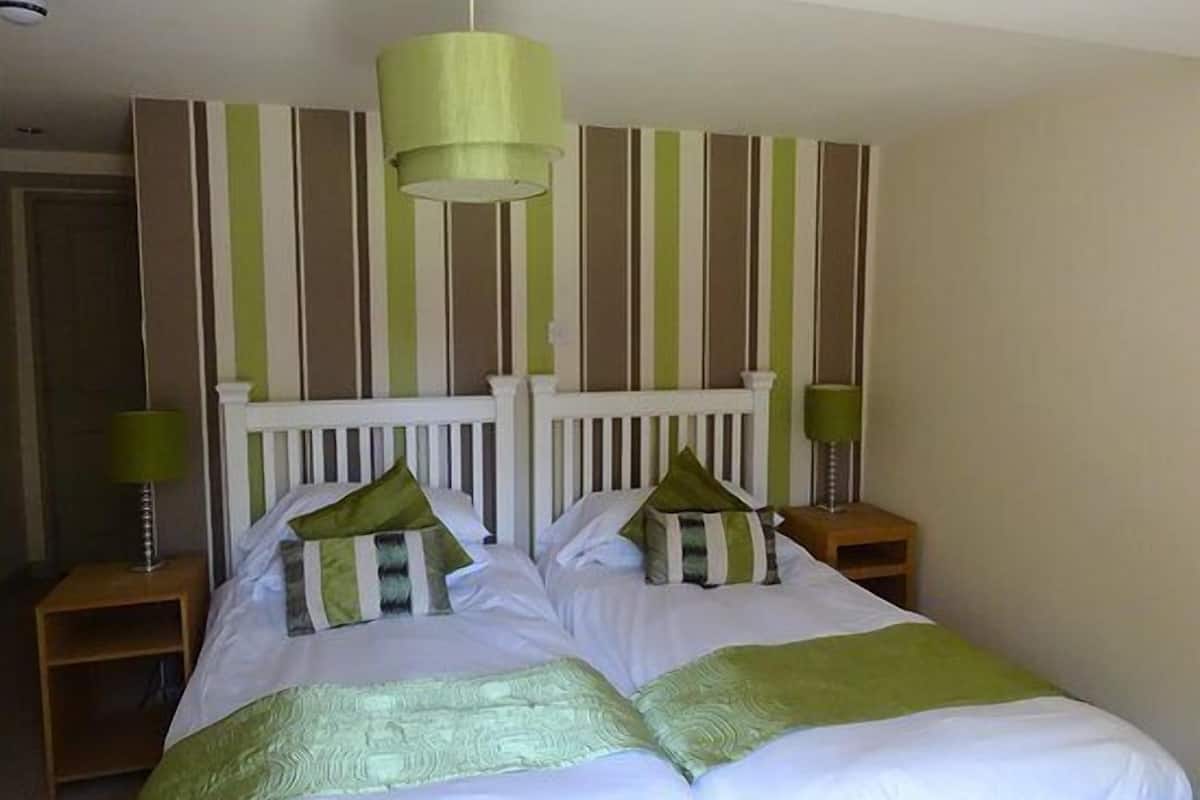 A neatly made bed with green and white bedding, a white headboard, and a green pendant light.