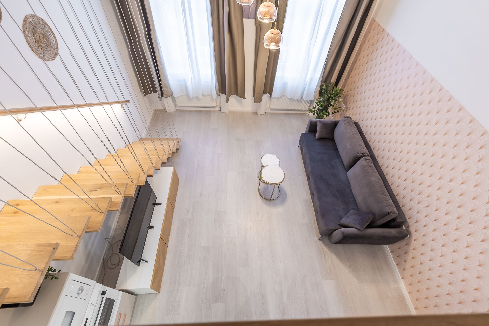 A modern living room with a sofa, a coffee table, and a TV. There is a staircase with wooden steps and a wall-mounted TV.