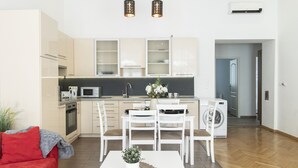 A modern kitchen with white cabinets, a dining area with a white table and chairs, and a red couch in a bright living space. - Real Apartments Revay (Budapest)
