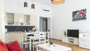 A modern apartment with a kitchen, dining area, and living room. It includes a sofa, a coffee table, a TV, and a painting on the wall. - Real Apartments Revay (Budapest)