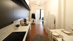 Une cuisine moderne avec des meubles sombres, une cuisinière noire et un plan de travail blanc. On y trouve un évier, un lave-linge et un coin repas avec une table mise pour deux personnes.