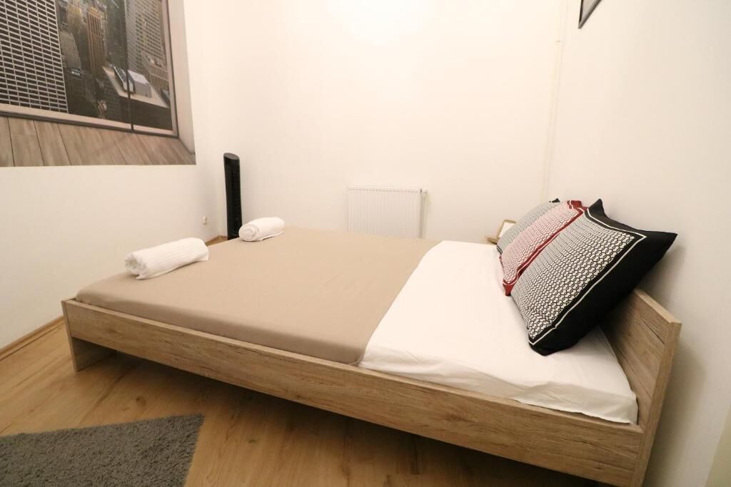 A single bed with a wooden frame, a beige mattress, a white pillow, and a patterned pillow.