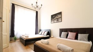Une chambre d’hôtel avec deux lits, une grande fenêtre avec des rideaux, un lustre et un tableau représentant un paysage urbain accroché au mur.