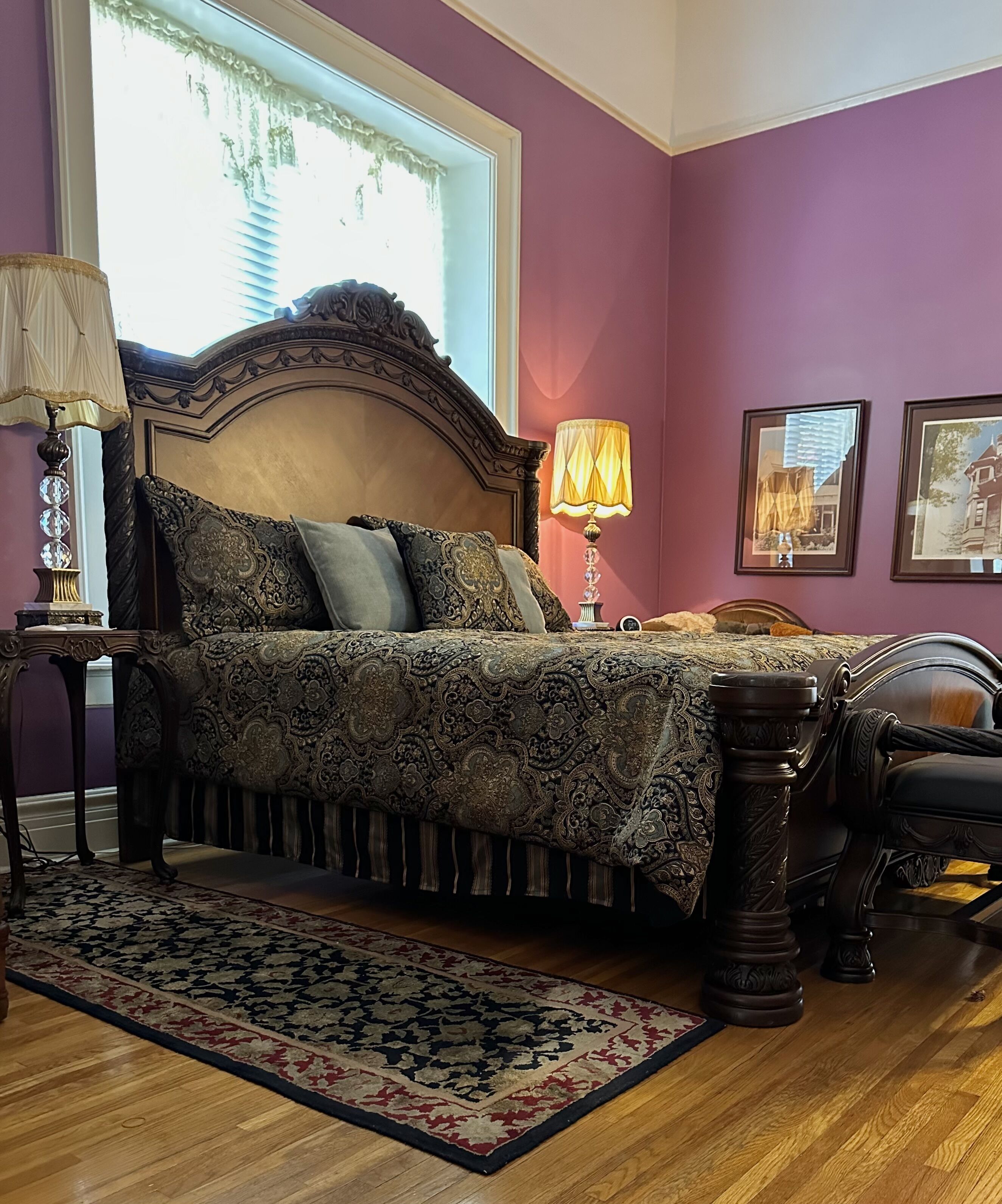 Een slaapkamer met een groot bed, een houten nachtkastje, een lamp en een vloerkleed.