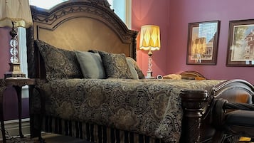 Een slaapkamer met een groot bed, een houten nachtkastje, een lamp en een vloerkleed.