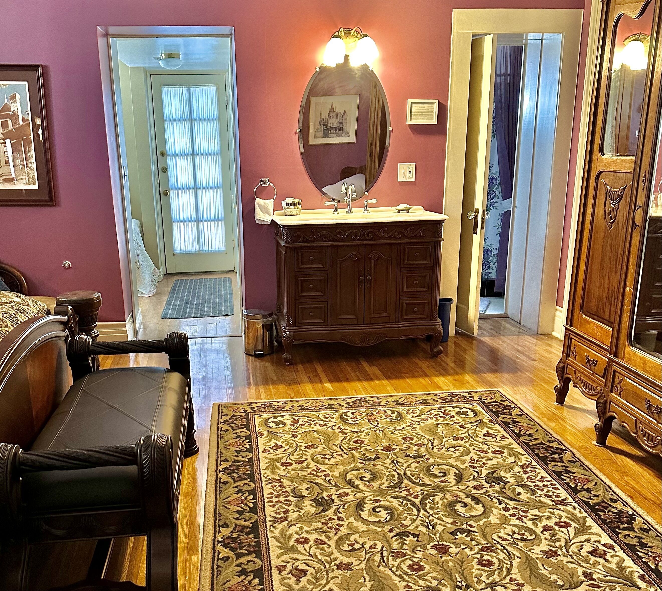 A living room with a wooden floor, a large rug, a sofa, a wooden cabinet, and a door leading to another room.